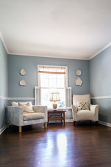 Light blue sitting room with two cream colored chairs and decorative plates on the wall and a small accent table