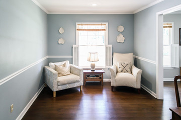 Fototapeta na wymiar Light blue sitting room with two cream colored chairs and decorative plates on the wall and a small accent table