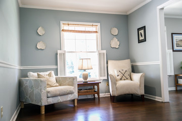Light blue sitting room with two cream colored chairs and decorative plates on the wall and a small accent table