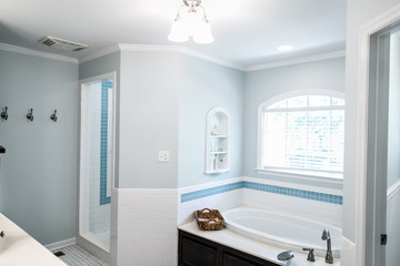 bathtub area of 1950's style bathroom with tile floor and dark brown cabinets in white and blue accents wit a window and natural light
