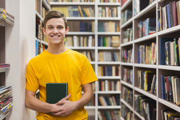 Cheerful male student standing between bookshelves in library