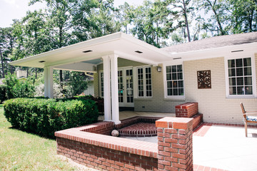 Back Rearview of exterior white cream brick 1950's house with black shutters and a large porch patio and also with a lawn lot with curb appeal