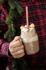 Man in plaid shirt holding mason jar with hot chocolate on red background. Male hands with Presents...