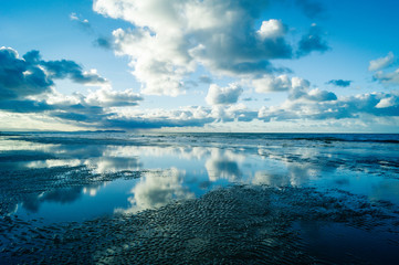 Reflections in the beach of a cloudy sky