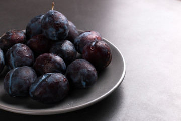 Fresh appetizing plums in a gray bowl, summer concept, copy space.