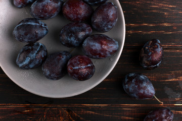 Fresh appetizing plums in a gray bowl, summer concept, copy space.