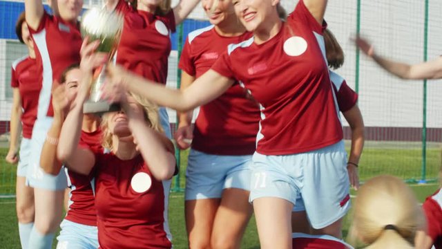 Happy women in soccer sportswear getting Cup, celebrating win and hugging each other