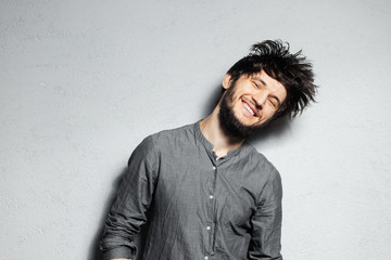 Obraz premium Portrait of young happy bearded guy with disheveled hair on grey background.