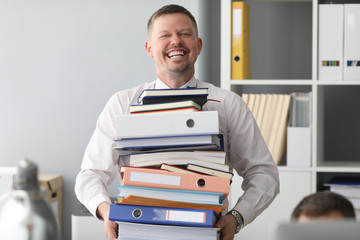 Happy office worker carry huge heavy pile of paper files to work with portrait. Overtime job for...