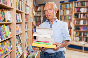 Portrait of elderly male holding pile of books in bookshop