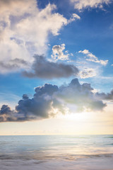 Naklejka na ściany i meble the sun in clouds. the sun shines through the dark gray clouds, the light is reflected in the calm blue sea, a beautiful landscape. Vertical photo.