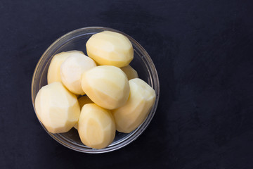 Top view of heap raw peeled potato in glass bowl on black background
