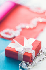 Women fancy gift. Closeup of red box with white ribbon bow and jewelry pieces on blur background. Copy space.