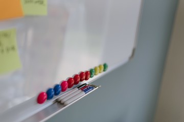 Closeup shot of a whiteboard with colorful pins and three markers on its tray shelf