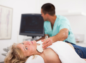 Obraz na płótnie Canvas Woman undergoing examination thyroid lying by man doctor with ultrasonic device