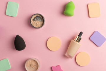 Sponges, a beautiful blender for applying foundation or powder and a bottle of concealer. Flat lay on a pink background, copy space.