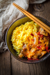 Saffron rice with pieces of chicken and vegetables on wooden table.