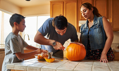 hispanic american family carving pumpkin into jack o lantern at home