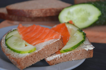 Healthy breakfast. sandwich with salmon and cucumber, brown bread and butter on a wooden background.