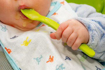 Baby holds a spoon and put it in his mouth with his little hand. Baby first soilds. Weaning.