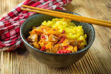 Saffron rice with pieces of chicken and vegetables on wooden table.