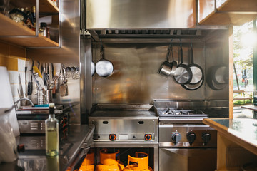 Small kitchen with stainless steel pots and pans in a rustic indoors restaurant with an open terrace at sunset. Clean and empty - obrazy, fototapety, plakaty