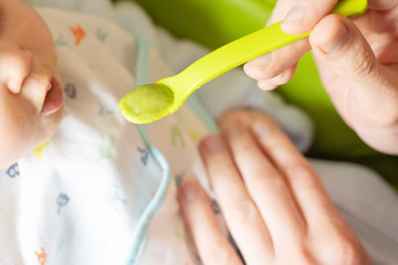 Adultt feeds little baby broccoli puree with a spoon. Baby first soilds. Weaning.