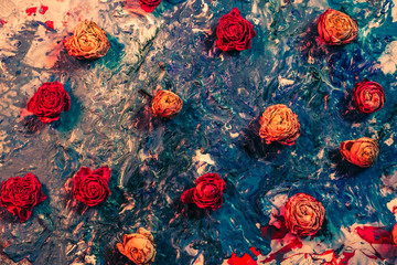 Abstract floral art background. Flat lay arrangement of red and orange dried rose buds on smeared blue paint.