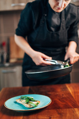 Female chef plating fried leeks on a toasted bread