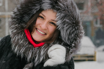 A cute Asian girl in a fluffy fur hat bowed her head and smiles.