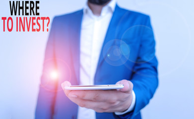 Word writing text Where To Invest Question. Business photo showcasing asking about where put money into financial schemes or shares Business concept with man holding mobile phone with touch screen