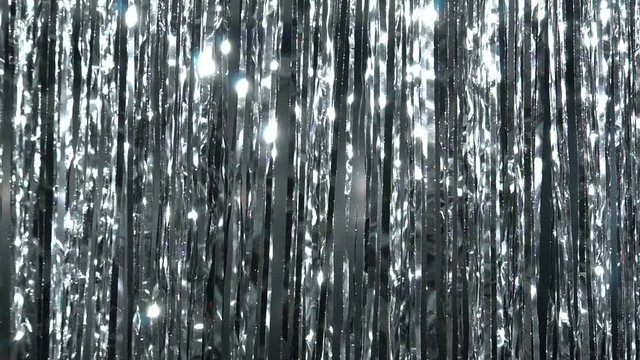 Silver rain from tinsel. Dynamic background in shining lights and sparkling particles. Beautiful silver background with shiny silver glitter sparkles. Festive mood. Christmas or holiday theme