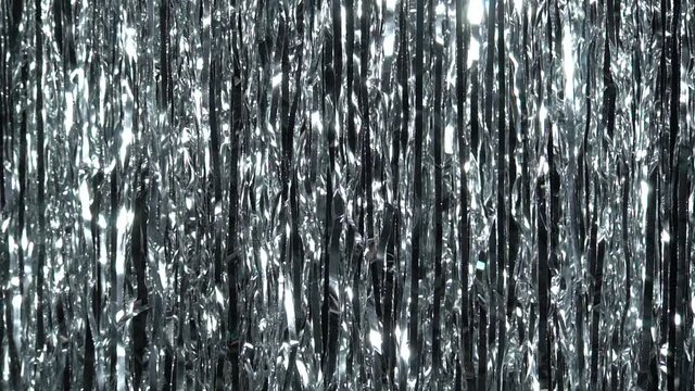 Silver rain from tinsel. Dynamic background in shining lights and sparkling particles. Beautiful silver background with shiny silver glitter sparkles. Festive mood. Christmas or holiday theme
