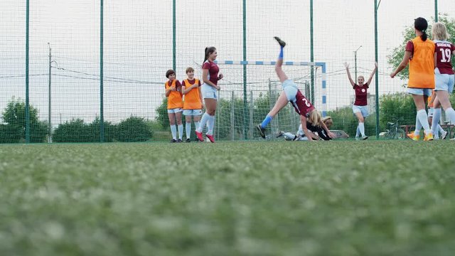 Female soccer player shooting goal, celebrating it, handspringing and hugging her team while goalkeeper falling on grass and feeling sad in background