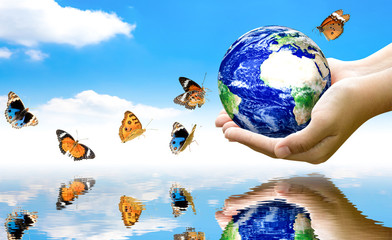 Woman hands holding world or globe above the river with water reflection with butterfly on earth...