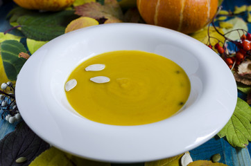 pumpkin soup in white plate wooden background with leaves