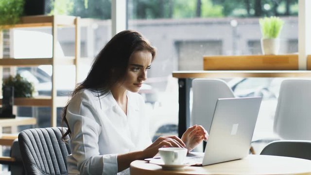 confused and baffled woman typing on laptop in cafe