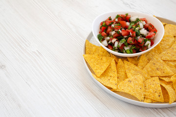 Pico de Gallo with gluten free tortilla chips on a white wooden background, side view. Copy space.