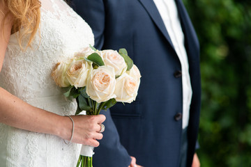 Bride and groom in the park. A bouquet of roses in the hands of the bride. Close-up