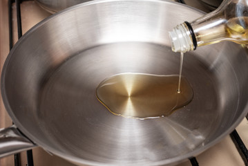Olive oil is poured onto a stainless steel pan