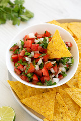Pico de Gallo with gluten free tortilla chips on a white wooden background, side view. Close-up.