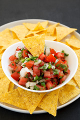 Pico de Gallo with gluten free tortilla chips on a black background, low angle view. Close-up.