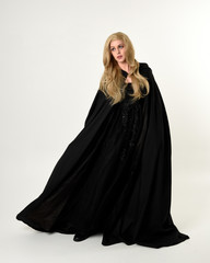 full length portrait of blonde girl wearing long black flowing cloak, standing pose  with  a white studio background.