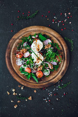 salad on a round wooden cutting board. Ingredients: soft-boiled egg, radish, cherry tomatoes, greens, red onions, arugula, dill, parsley, mint, walnuts, spices, cheese