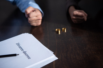 partial view of couple at table with divorce documents and rings