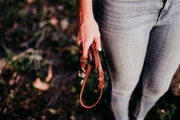 beautiful caucasian woman holding a brown leather dog leash at sunset in countryside. Pets and lifestyle outdoors. close up view