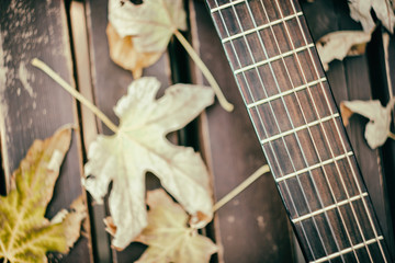 Close-up view of a fragment of acoustic classical guitar with fall maple leaf on wooden background. Autumn live concert concept.