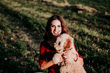 beautiful caucasian woman with her cute brown poodle dog at sunset in countryside. Pets and lifestyle outdoors