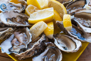 A dozen oysters and a lemon on a plastic plate eating outdoors near the sea