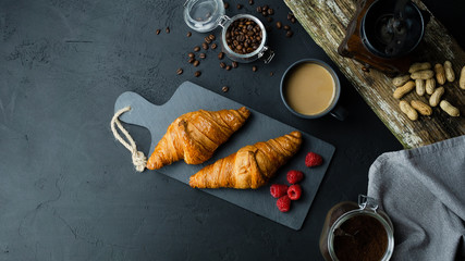 Rogale croissant leżące na ciemnej desce w otoczeniu malin i kawy. Ciemne tło, widok z góry. - obrazy, fototapety, plakaty